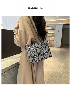 Detail showing snake pattern faux leather texture and black metal chain of the handbag