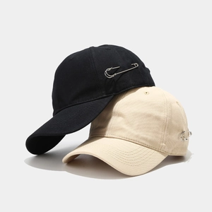Black and beige minimalist baseball caps with silver metal pin detail on cotton fabric