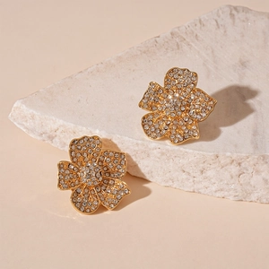 Macro shot of gold-plated flower earrings with sparkling rhinestones on stone background