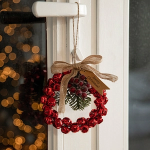 Christmas wreath with red bells, pine needles and Merry Christmas tag on white door