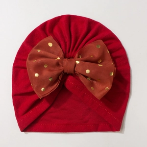Close-up of red infant turban hat featuring a brown bow with golden polka dots