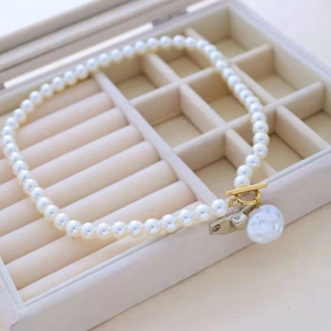 Collier de perles élégant avec fermoir doré et pendentif baroque dans un écrin beige