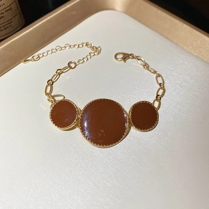 Gros plan du bracelet à maillons dorés avec trois pendentifs circulaires en émail brun