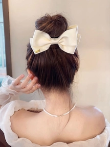 Close-up of cream bow hair claw clip in satin fabric with a small gold brand tag