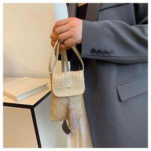 Detail of hand-woven straw crossbody bag with golden button and tassel accent