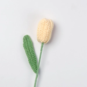 Detail einer handgehäkelten Tulpe aus blassgelbem Garn mit grünen Strickblättern