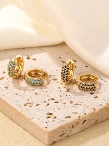 Détail de créoles de luxe dorées avec incrustations de zircon turquoise et noir sur pierre