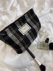 Detail of checkered wool makeup bag with metal zipper on a white fabric background