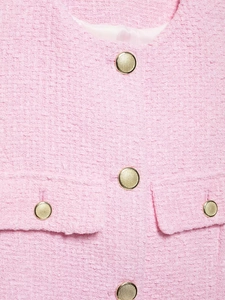 Détail de la texture tweed rose avec boutons en métal doré et coutures raffinées sur la veste