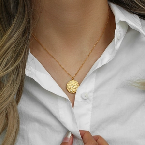 Dettaglio della collana a moneta d'oro con perla bianca e strass indossata dal modello