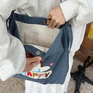 Detail view of the canvas tote bag showing stripe pattern, magnetic snap, and inner pocket