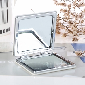 Detailed view of an open square silver metal folding compact mirror with double-sided glass