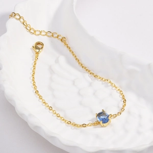 Detail of a gold plated bracelet with a blue round cut zircon and lobster claw clasp