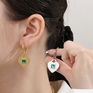 Detail of heart stud earrings in gold and silver finish with emerald green zircons