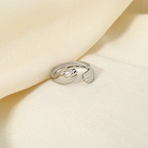 Bague mains qui s'enlacent en argent poli sur un tissu texturé beige chaud