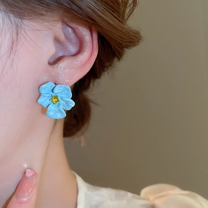 Macro shot of light blue floral stud earring with yellow gemstone and enamel petals