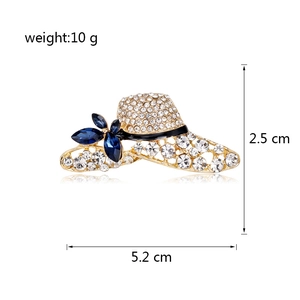 Golden hat brooch with sparkling rhinestones and blue crystal flower on white background