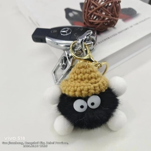 Macro shot of cute black plush fuzzy ball keychain with yellow knit hat and gold clasp