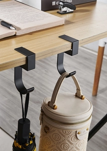 Detail showing the black U-shaped metal desk hook holding a bag and an umbrella