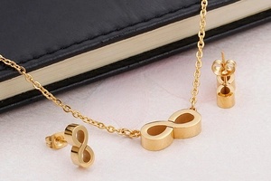 Detailed view of a gold infinity symbol necklace and earring set on a pink marble surface