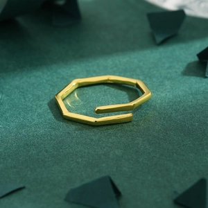 Minimalist geometric octagon gold open ring on a dark green surface with modern props