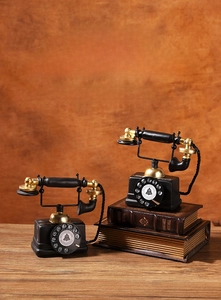 Close-up of vintage black and gold telephone models on retro books in a warm rustic setting