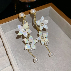 Macro detail of long gold earrings featuring white 3D flowers with pearls and rhinestones