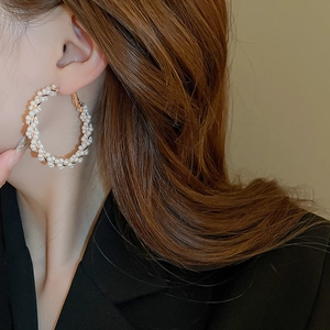 Gros plan sur d'élégantes créoles en perles tressées dorées portées par un mannequin
