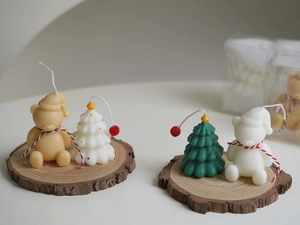 Close-up of mini Christmas bear and tree candles on a rustic wooden slice base