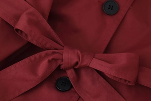 Gros plan du trench bordeaux croisé montrant la texture sergée et le nœud à la taille