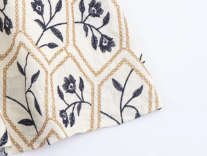 Detail der eleganten Goldkettenstickerei und blauen Blumenmuster auf beigem Stoff