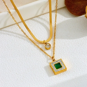 Detailed macro view of layered gold necklace with emerald pendant and snake chain