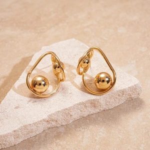 Details von verdrehten goldenen Metallohrringen mit Kugelanhänger auf Naturstein