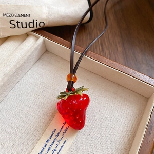 Close-up of red resin strawberry pendant with green leaf detail and brown leather cord