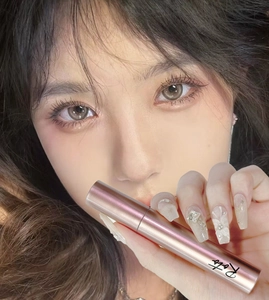 Close-up of rose gold mascara wand held by a model for a volumizing lash look
