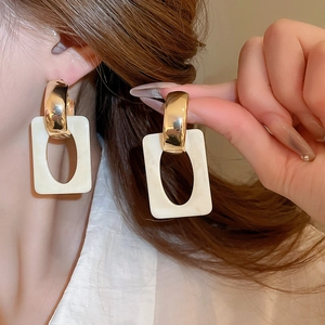 Close-up of geometric gold metal and cream resin earrings worn on model for detail