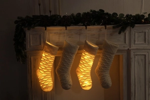 Detail of four cream knitted Christmas stockings with fish scale texture and warm LED lights