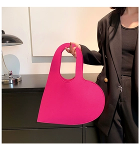 Detail view of bright pink heart-shaped felt handbag held by a person in a black suit