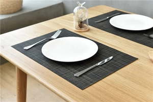 Close-up of thick dark grey woven PVC placemat on a wooden table with elegant tableware