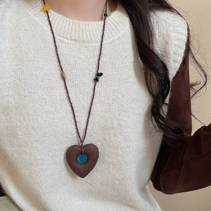 Detail view of ethnic heart pendant necklace with dark stone beads on white knit sweater