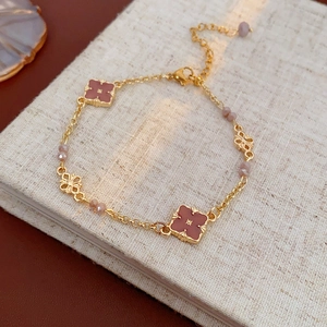Detailed view of a vintage gold bracelet with red clover motifs and pink beads on a book