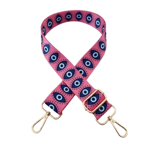 Detail of adjustable polyester bag strap with pink evil eye patterns and gold hardware