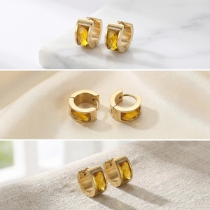 Detail view of gold stainless steel hoop earrings with amber glass stones on marble