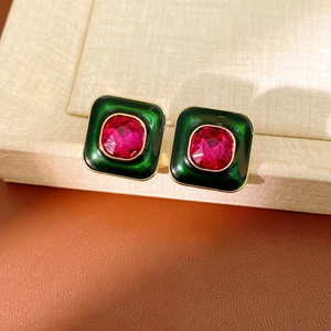 Close-up of vintage square earrings with green enamel and red gems on a display pad