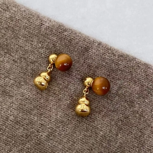 Detailed close-up of gold gourd earrings with tiger eye beads on knit background