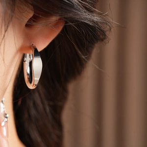 Close-up of a minimalist silver oval hoop earring worn on a model's ear