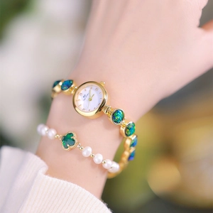 Close-up of golden jewelry watch with green stone inlays and a pearl clover bracelet