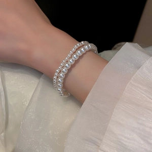 Double-layer pearl bracelet with glossy white beads on wrist with fabric background