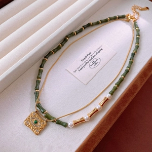 Détail du collier doré avec pendentif vert émeraude et perles sur un plateau à bijoux