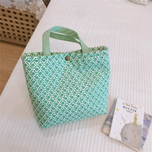 Top-down view of a floral canvas lunch bag with green handles and a vintage metal button
